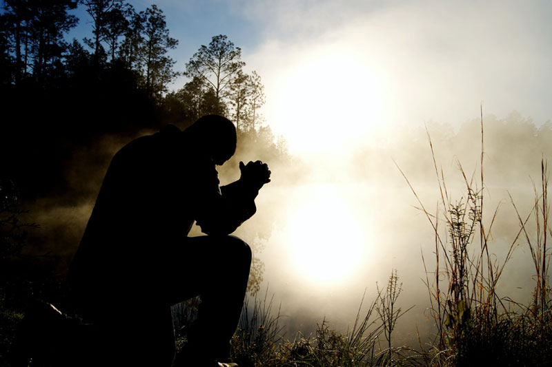 man kneeling in prayer on a lake shore